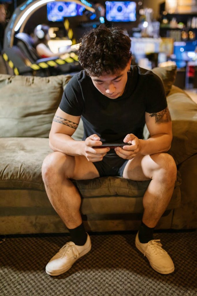 A young man intensely focused on playing a game on his smartphone while sitting indoors.