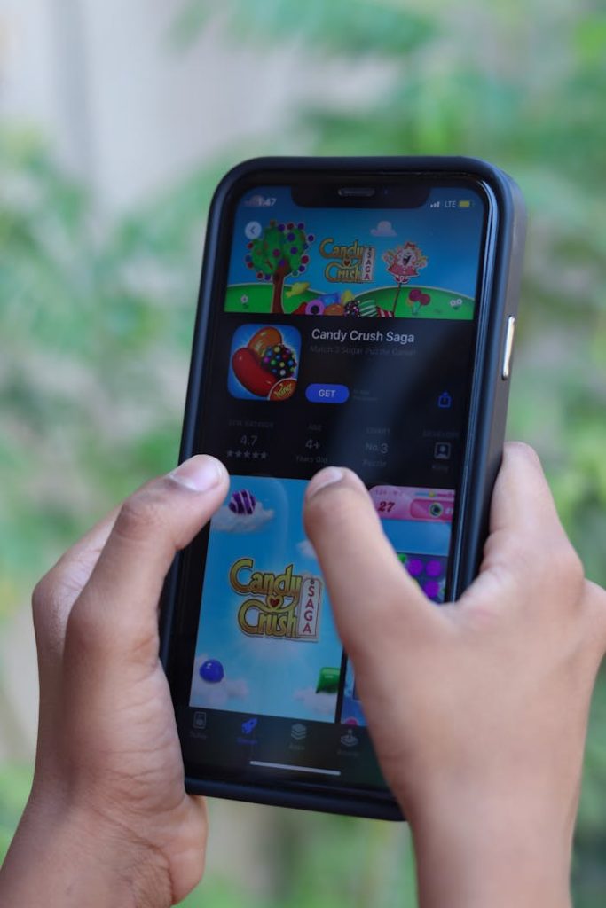 Close-up of hands holding a smartphone playing Candy Crush Saga outdoors.