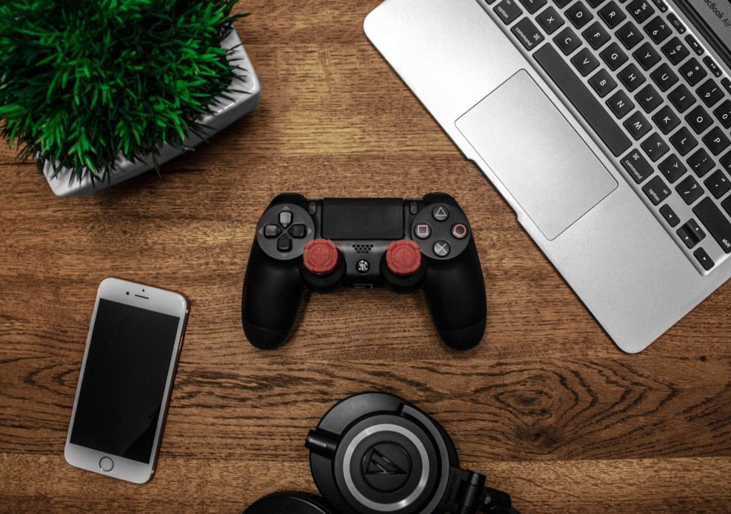 A flat lay photo showcasing a gaming console, laptop, smartphone, and headphones on a wooden tabletop.